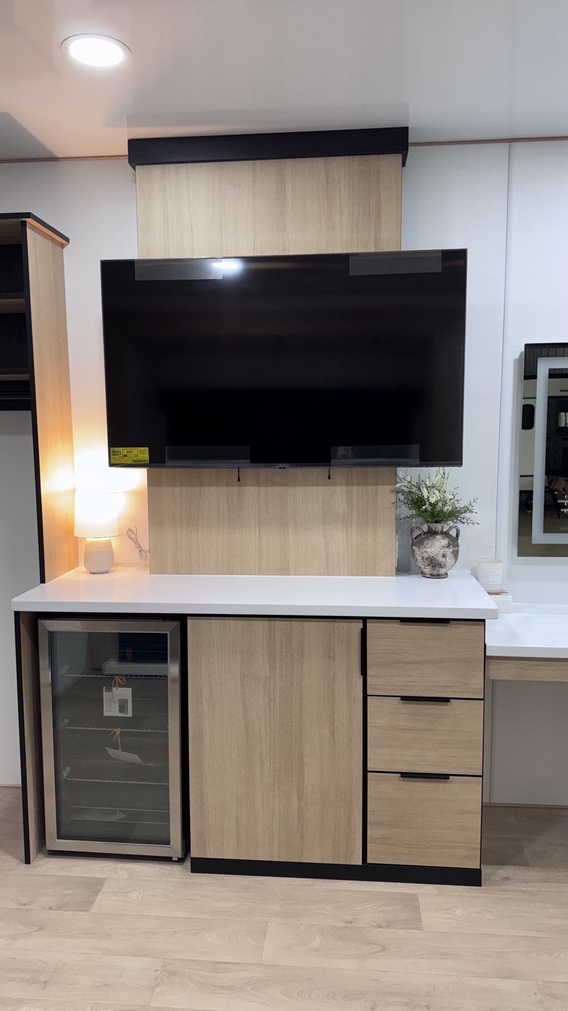 Wall-mounted TV above wood-grain cabinetry with built-in beverage fridge in the Model A media wall