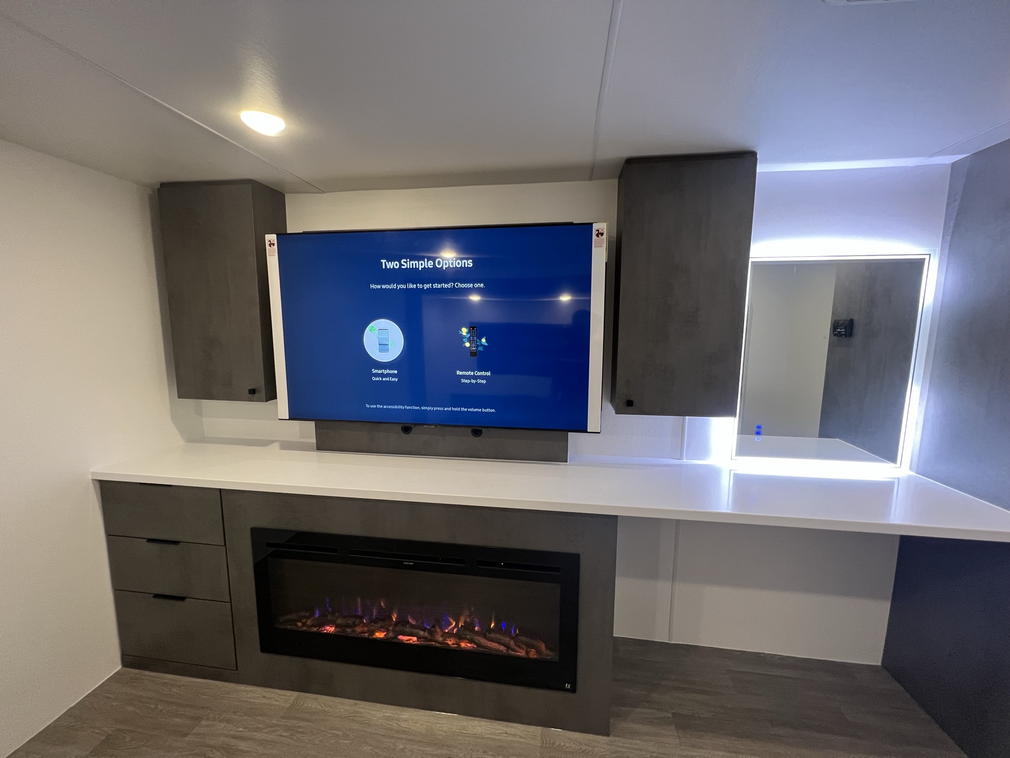 Centered view of the linear electric fireplace, soundbar-equipped TV, and backlit vanity mirror in Model C