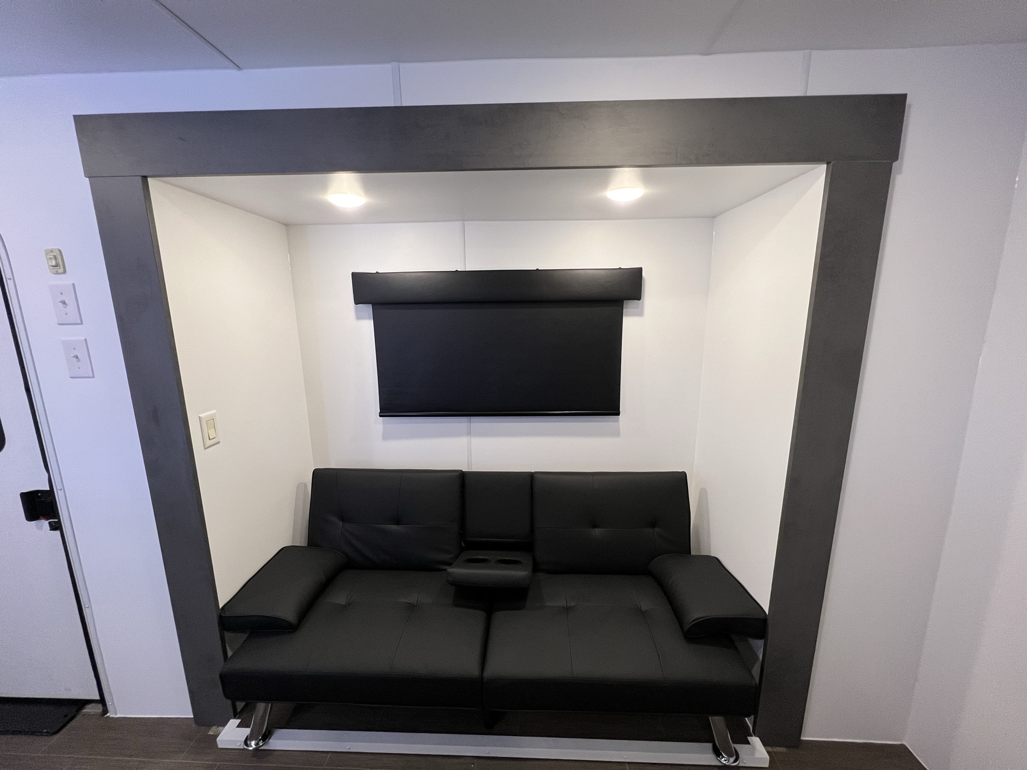 Convertible black leather sofa framed by a charcoal slide-out box with overhead downlights