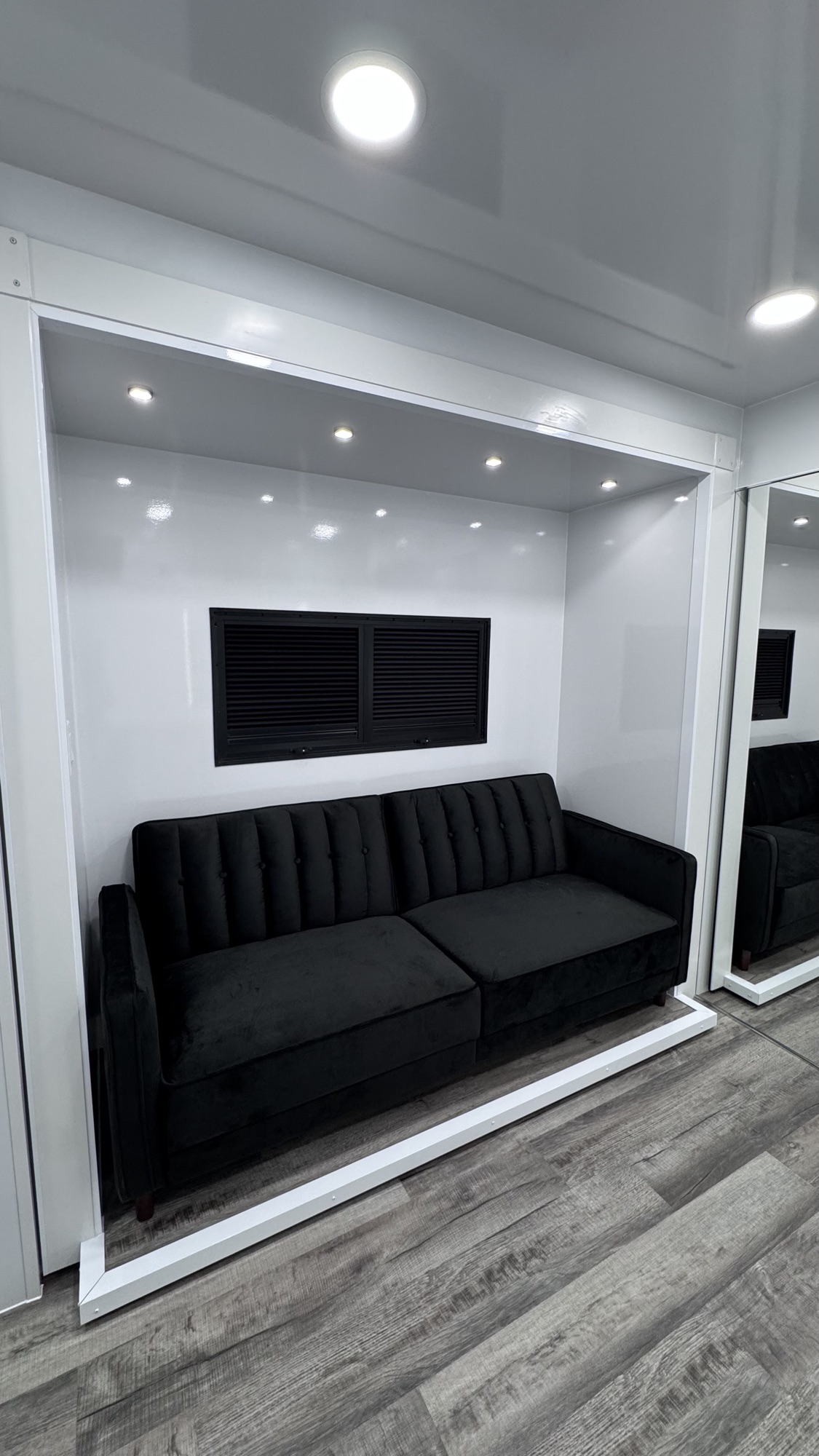 Tufted black velvet sofa in a recessed alcove with white framing and a vented storage panel above