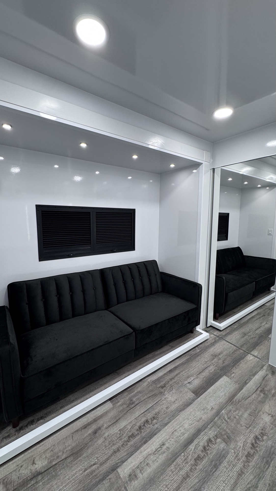 Talent lounge featuring a black tufted sofa under recessed lighting with a full-length mirror reflecting the space