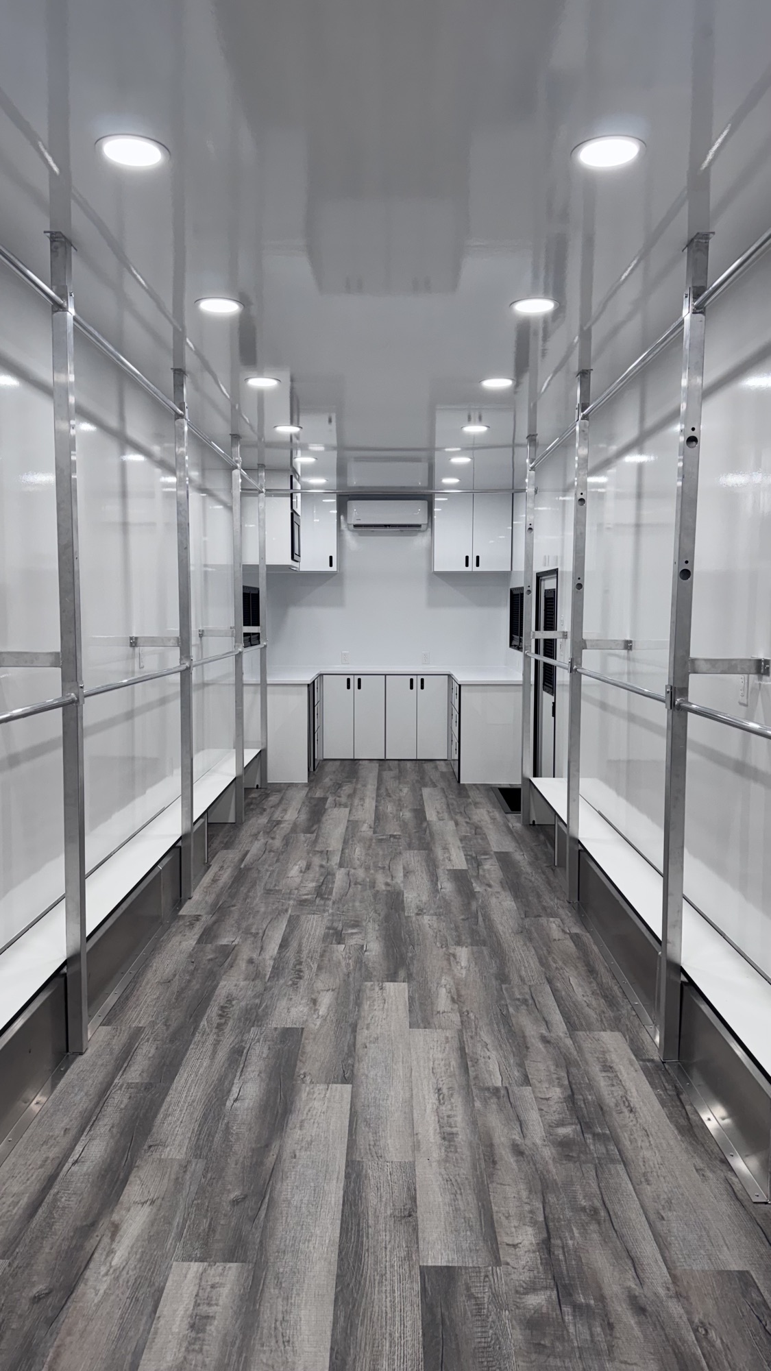Interior of wardrobe trailer with dual hanging-rack runs, recessed lighting, and a rear prep counter