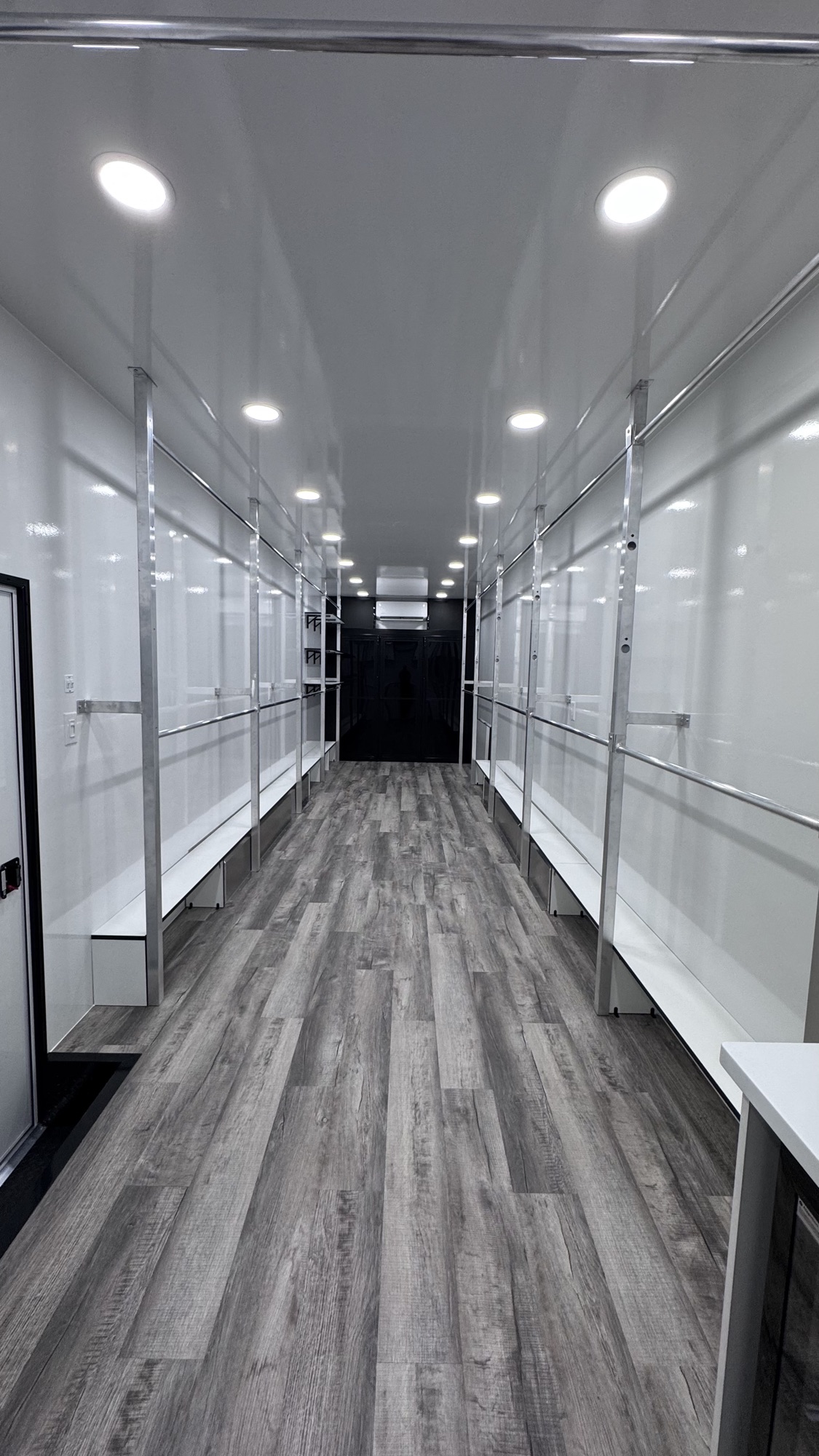 Long view inside the wardrobe trailer showing rows of hanging garment racks and aluminum support posts